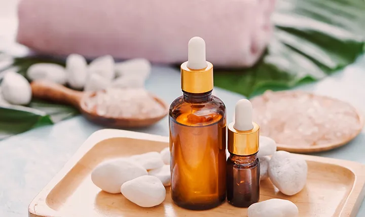 Two brown glass dropper bottles on a wooden tray with white stones, a leaf, and sea salt.